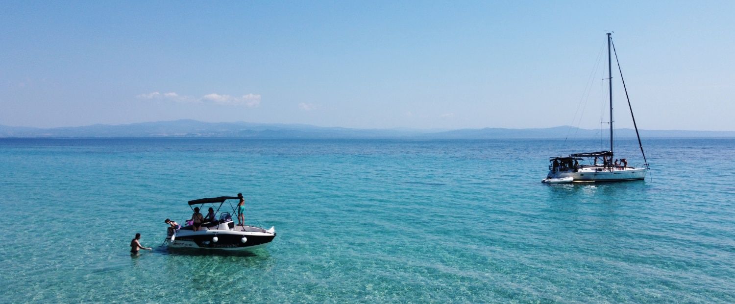 Rental boat and sailing yacht anchored in turquoise water in Halkidiki